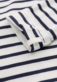 Camiseta de algodón a rayas en azul marino y blanco, con mangas enrolladas y tejido texturizado, con costuras visibles y un detalle de etiqueta en forma de lazo.