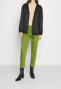 Czarna, lekka kurtka z elastycznymi mankietami, zestawiona z zielonymi spodniami prostymi i czarnymi botkami za kostkę. Beżowa bluzka pod spodem.