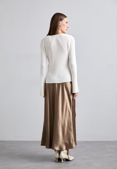 Λευκό ριμπ μακρυμάνικο τοπ συνδυασμένο με καφέ σατινένια μακριά φούστα. Το τοπ έχει εφαρμοστή σχεδίαση, ενώ η φούστα είναι αέρινη και απλή. Οι ελεφαντόδοντες ψηλές μπότες ολοκληρώνουν το σύνολο.