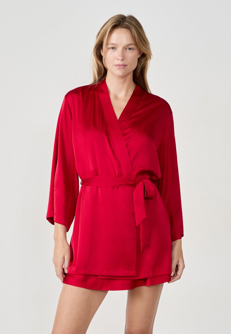 Accappatoio in raso rosso con maniche lunghe e cintura in vita. Il tessuto ha una consistenza liscia e il design presenta una scollatura a V e una lunghezza corta.