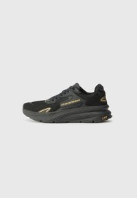 Black athletic sneaker featuring a textured upper, padded collar, lace-up design, and a thick rubber sole. Gold accents detail the side.