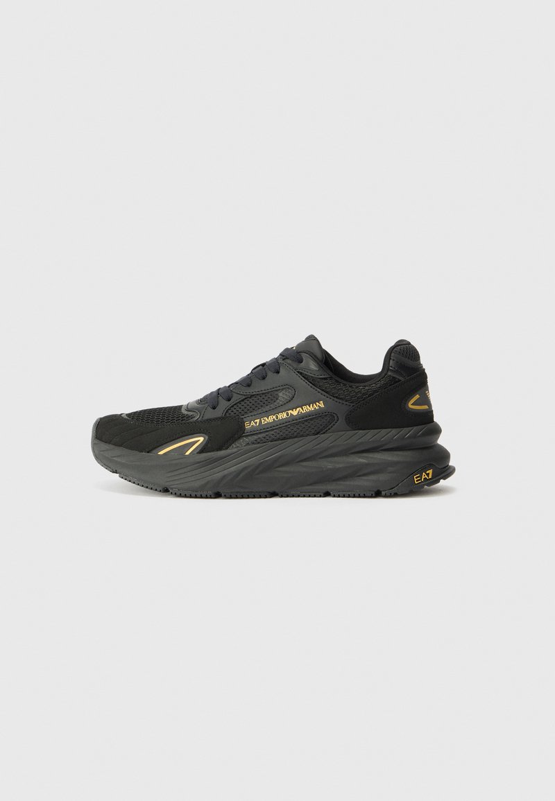 Black athletic sneaker featuring a textured upper, padded collar, lace-up design, and a thick rubber sole. Gold accents detail the side.