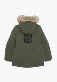 Parka verte avec capuche en fausse fourrure, présentant un imprimé graphique noir dans le dos. Le matériau semble lisse, avec un léger éclat et un design isolé.