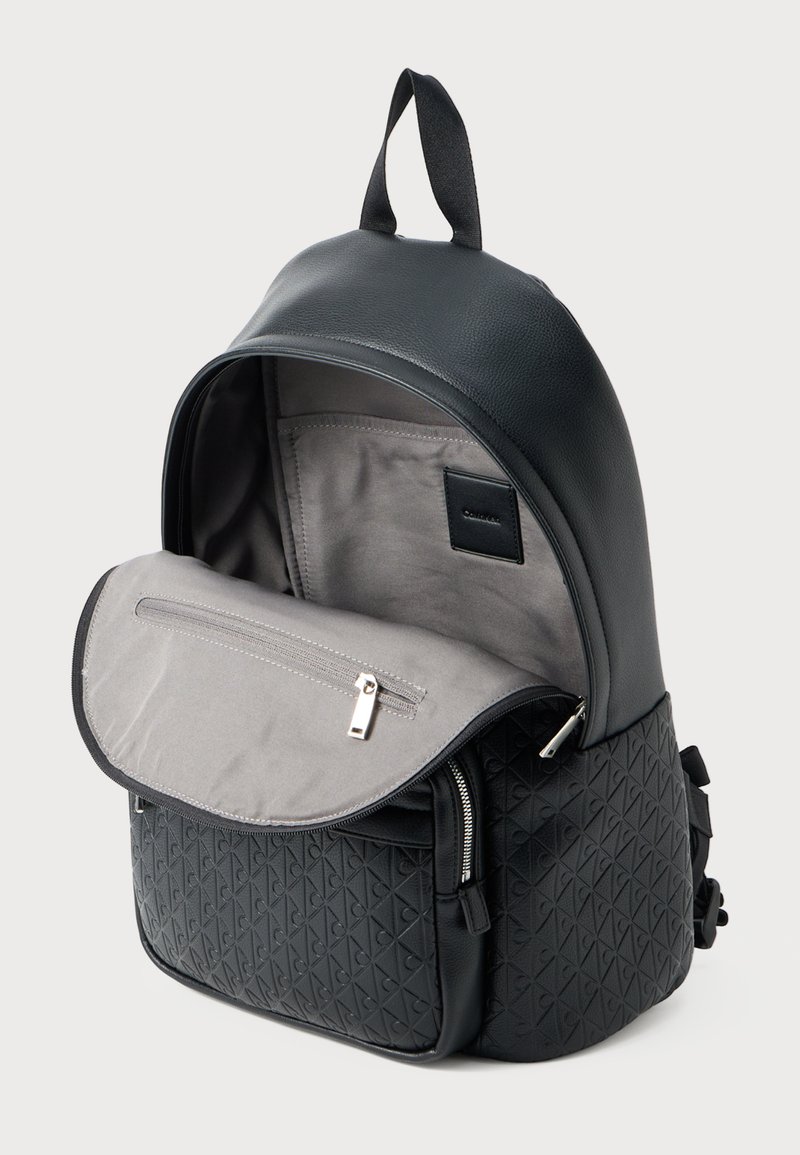 Black leather backpack featuring a textured bottom with a diamond pattern, a grey interior, one zip pocket, and a top handle.