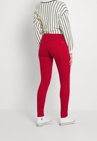 Persona vestida con pantalones ajustados rojos, zapatillas Converse de caña alta blancas y un suéter blanco con rayas verticales negras, mostrado desde atrás.