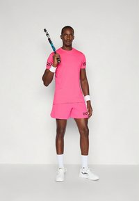 Ljusrosa tränings-T-shirt med korta ärmar och shorts med svart "BORG"-text. Vita handledsband och skor kompletterar den sportiga looken. Tennisracket ingår.
