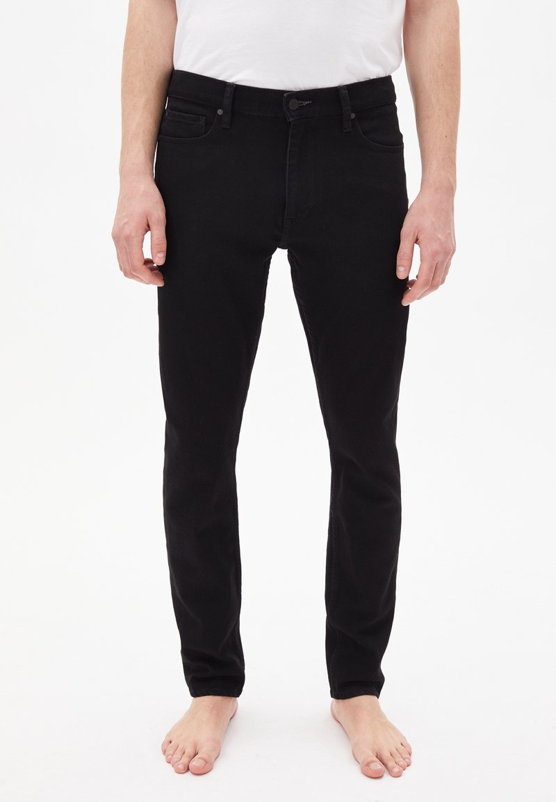 Jeans en denim noir au design ajusté, avec cinq poches et une fermeture à bouton. Le tissu a une texture lisse et un léger stretch.