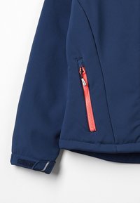 Mørkeblå softshell-jakke med en kontrasterende orange lynlås og velcro-manchetter. Har en lynlåslomme på siden. Glat tekstur.