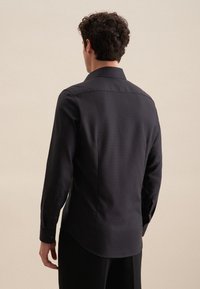 Camicia nera a maniche lunghe con colletto a punta, texture liscia e polsini con bottone. Caratterizzata da un orlo dritto e dettagli sottili sulla parte posteriore.