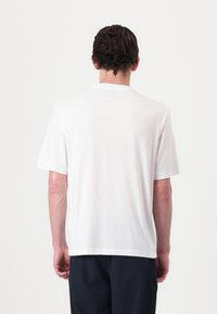 Hvid bomulds t-shirt med afslappet pasform, korte ærmer og en simpel rund halsudskæring, vist fra ryggen mod en ensfarvet baggrund.