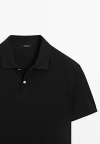Polo noir à manches courtes avec col et patte de boutonnage à deux boutons, étiquette de marque visible à l’intérieur de l’encolure.