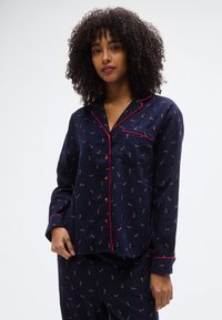 Pyjama bleu marine en tissu doux, avec un motif à accents roses, fermeture à boutons sur le devant et une poche poitrine.