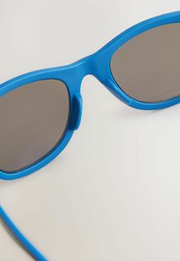 Occhiali da sole in plastica blu con lenti scure, caratterizzati da una texture liscia e un design avvolgente, che mostrano un aspetto moderno e sportivo.