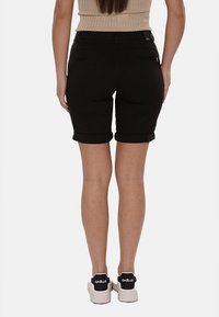 Shorts in denim nero con un design aderente, orli risvoltati e due tasche posteriori. Indossati con sneakers bianche con un accento nero.