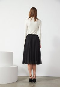 Gonna nera plissettata con una texture fluida, dotata di una vita elastica. Abbinata a un elegante top bianco a maniche lunghe e scarpe con tacco alto.