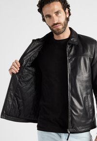 Zwarte leren jas met een ritssluiting aan de voorkant en een gewatteerde binnenvoering, met een kraag en zijzakken voor extra detail.