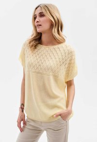 Jasnożółty sweter z krótkimi rękawami, z diamentowym wzorem w górnej części i gładką dolną częścią. Luźny krój.