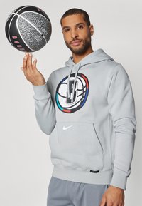 Pilkas džemperis su dideliu daugiaspalviu krepšinio logotipu, matoma kengūros kišenė ir mažas Nike logotipas priekyje. Juodas ir pilkas krepšinis yra sukamasis.