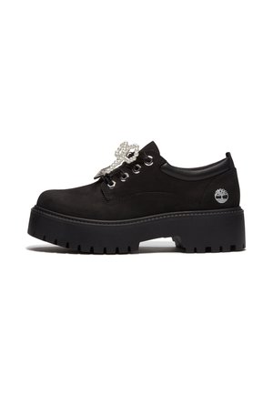 Chaussure à plateforme noire avec semelle épaisse à crampons, design à lacets, embellissement en perles sur les lacets et logo arbre Timberland sur le talon.