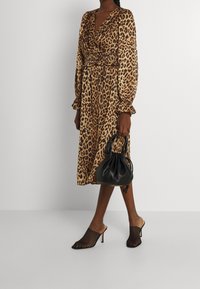 Lepardmönstrad klänning med långa ärmar, markerad midja och flödande tyg. Bärs med svarta nätklackar och en liten svart handväska.