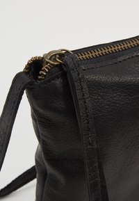 Borsa in pelle nera con superficie testurizzata, hardware con cerniera color oro e una sottile tracolla per il trasporto. Dettagli di cuciture multiple visibili.