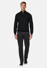 Melna zip-up džemperis, kas apvienots ar tumši pelēkiem biksēm un melnām kedām. Džemperim ir augsts apkakle un ribinātas piedurknes. Neitrāls fons.