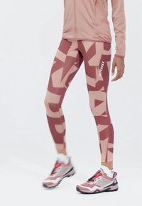 Legíny v růžových odstínech s geometrickými vzory, vysokým pasem, elastickým materiálem a bočním logem. Navrženo pro sportovní nošení.
