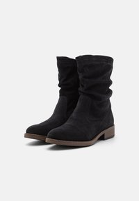 Black suede ankle boots with a slouchy design, round toe, low stacked heel, and visible stitching details. Subtle branding on the side.