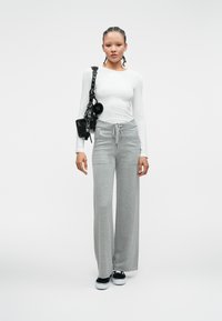 Szare, szerokie dresy z pasem do regulacji w talii, połączone z białą bluzką z długim rękawem. Czarna torebka na ramię, czarne sneakersy.