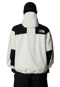White and black windbreaker jacket with a hood, featuring a back logo, elastic hem, and smooth texture. Color-blocked design enhances visual interest.