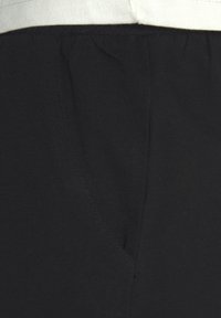 Schwarze Baumwoll-Jogginghosen mit strukturierten Oberflächen, ausgestattet mit einem elastischen Bund und einer Seitentasche mit subtilen Nahtdetails.