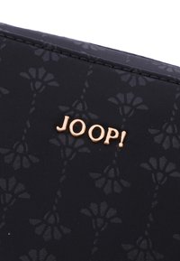 Tessuto nero a motivo floreale con una superficie liscia, caratterizzato da un prominente logo dorato "JOOP!" come dettaglio distintivo.