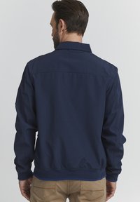 Navy blue jacket made of smooth fabric with a collar, elasticated cuffs, and waistband. Features a simple design without visible logos.