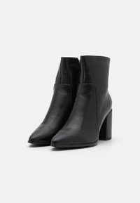 Paire de bottines en cuir noir avec bouts pointus, talons blocs et fermetures éclair latérales sur fond blanc.
