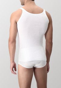 Canotta bianca a costine con spalline larghe, indossata su culotte bianche coordinate. Tessuto liscio e design aderente.