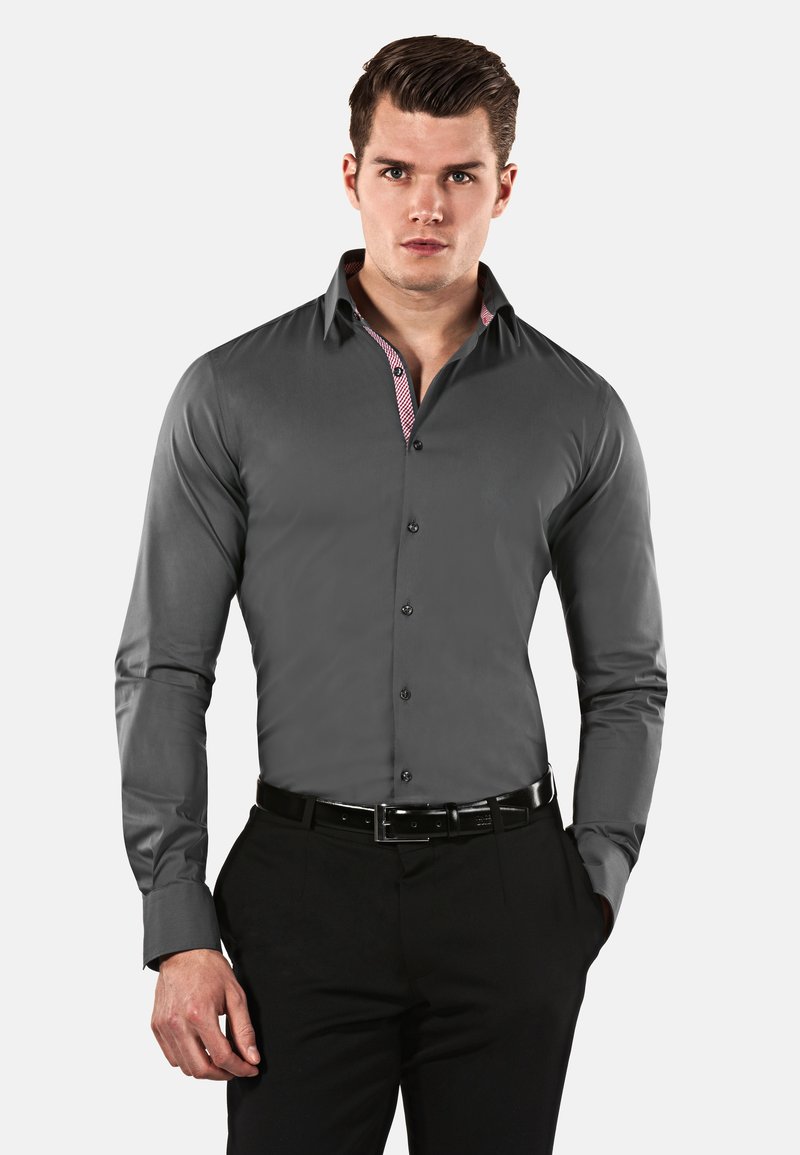 Camicia grigia a maniche lunghe realizzata in tessuto morbido, con colletto alla francese e un motivo a quadri all'interno del colletto. Indossata con pantaloni neri.