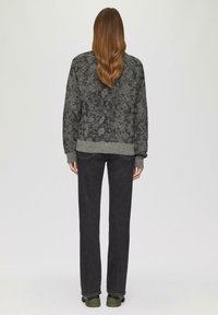 Grijze gebreide trui met een gemêleerd patroon, gecombineerd met donkere jeans en groene schoeisel. De trui heeft een geribde tailleband en manchetten.