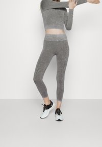 Graues Sportset bestehend aus einem enganliegenden Langarmoberteil und hochgeschnittenen Leggings mit kontrastierenden Nahtakzenten und glatter Textur.