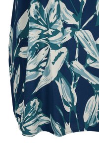 Tissu bleu avec un grand motif floral blanc et vert d'eau, montrant des pétales et des feuilles dans un design superposé.