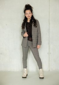 Grijze geruite blazer en bijpassende slim-fit broek, gedragen over een donkere top. Lichtgekleurde, veterschoenen tot de enkel met een chunky zool.