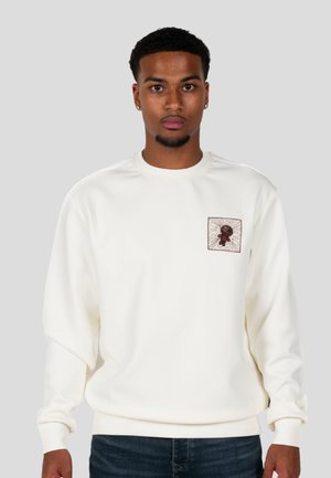 Sudadera blanca de manga larga, con un cuello redondo y un parche cuadrado bordado en el pecho con un detalle gráfico.