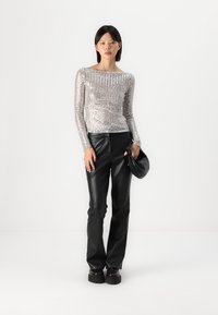 Ασημένια αμάνικη μπλούζα με παγιέτες και στρογγυλή λαιμόκοψη, συνδυασμένη με μαύρα παντελόνια από τεχνητό δέρμα με ψηλή μέση και μαύρα παπούτσια με χοντρό πάτο.