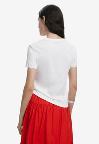 Hvid bomulds t-shirt med korte ærmer, der har en rund halsudskæring, parret med en rød, voluminøs, samlet nederdel. Rent design, ingen grafik.
