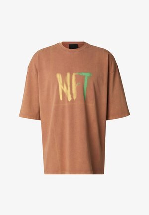 Maglietta a maniche corte oversize di colore ruggine, realizzata in morbido cotone, con testo grafico giallo e verde "NFT" sul davanti.