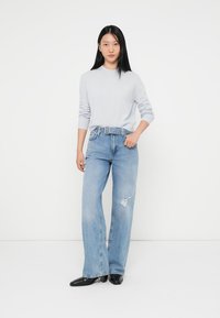 Ljusgrå tröja med långa ärmar, tillsammans med ljusblå vida jeans som har ett hål på vänster lår. Svarta spetstövlar.