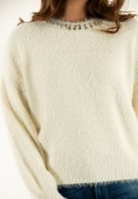 Maglione bianco e soffice con scollo rotondo arricchito da accenti di gemme trasparenti. Presenta maniche lunghe e una vestibilità morbida.
