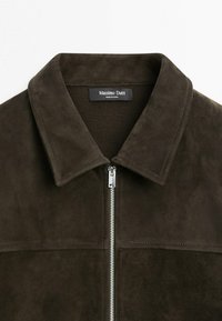Dunkelbraune Wildlederjacke mit spitzem Kragen und silbernem Reißverschluss vorn, mit dem "Massimo Dutti" Etikett im inneren Nackenbereich.