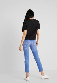 Černé zkrácené tričko v kombinaci s světle modrými džíny, které mají klasický střih a minimalistický design. Model má na sobě bílé tenisky.