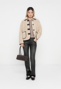Beige fleece jacket with black trim, button closures, and oversized pockets. Paired with dark jeans and a small brown handbag.