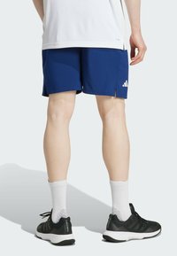 Blå träningstights med sidofickor, kombinerat med svarta sneakers och vita strumpor. Tightsen har Adidas-logotypen i vitt.